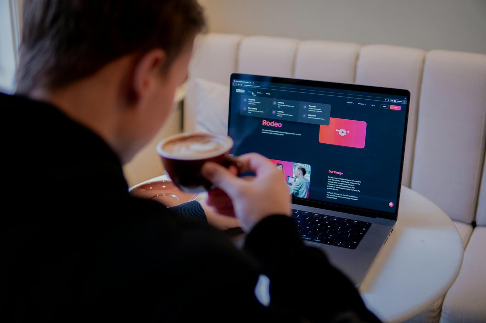 back view of a man sitting with a coffee cup and looking at a laptop screen